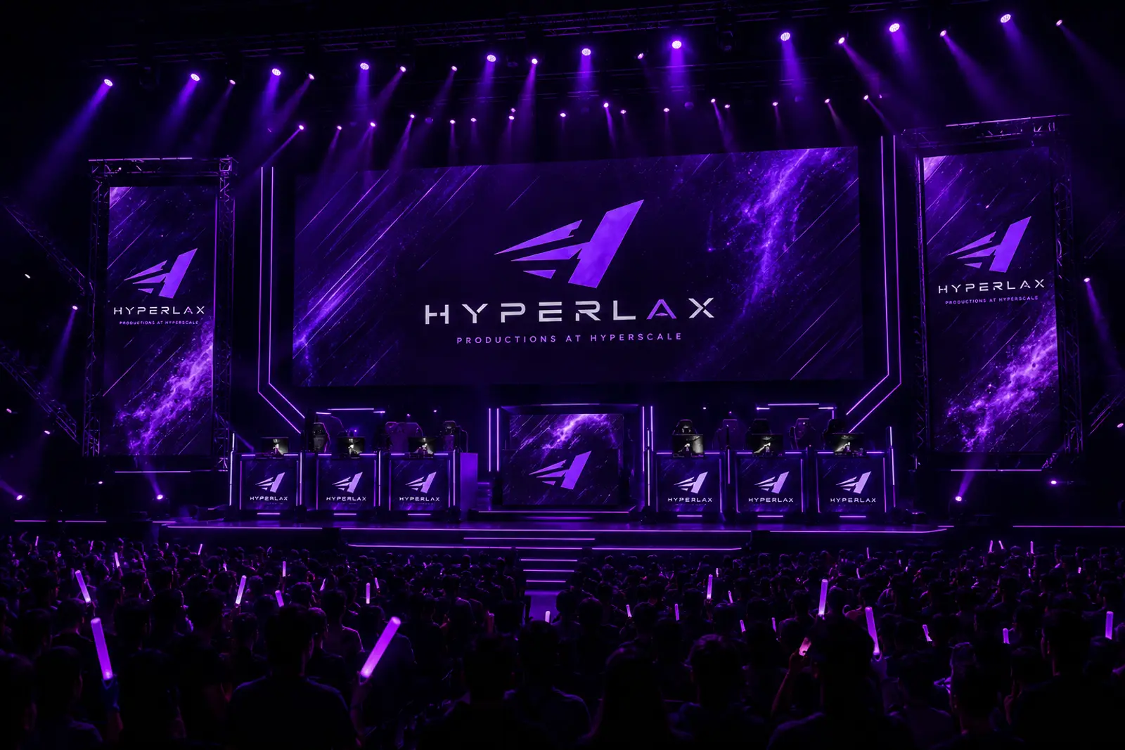 A Hyperlax-produced arena show: LED screens with the Hyperlax mark above a stage, purple beams over a full crowd